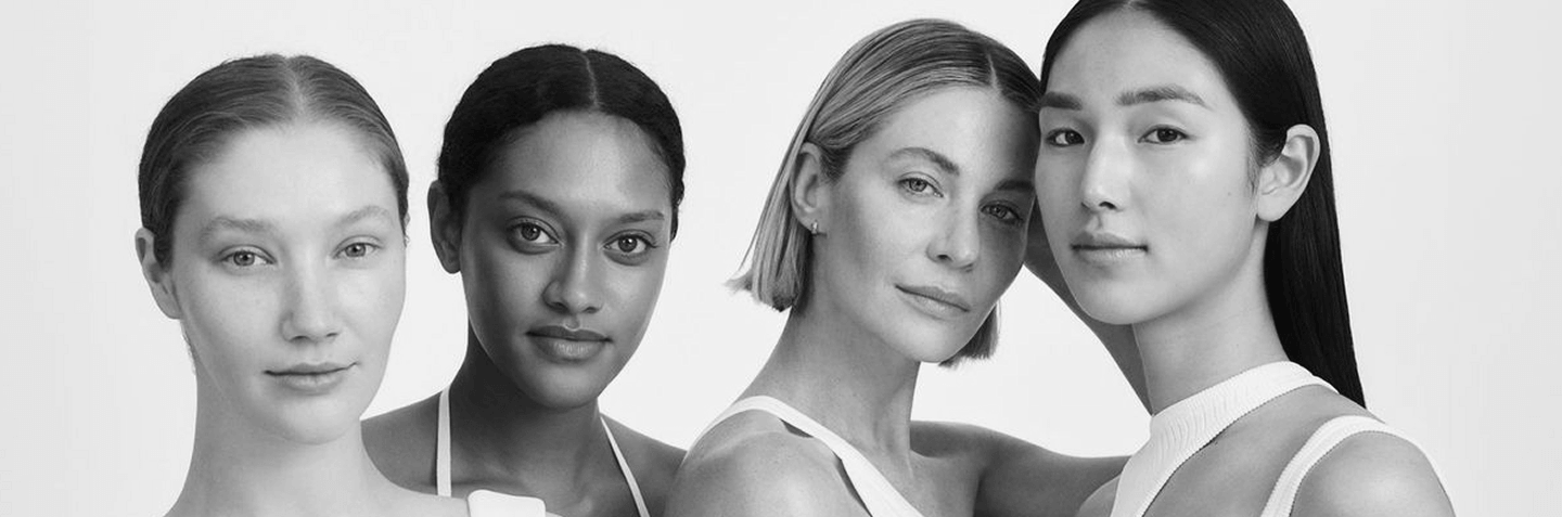 Four women of diverse backgrounds stand closely together against a plain background, all facing forward with neutral expressions.